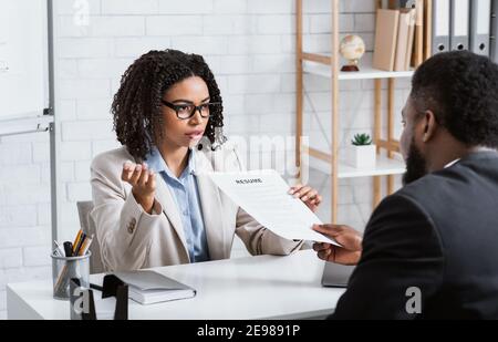 Serious personnel manager taking resume from young job applicant on work interview at modern company office Stock Photo