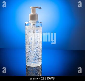 Cosmetic product for makeup remove. Clear liquid with small air bubbles on blue light backgroud. Bottle with dispenser. On dark surface background. Stock Photo