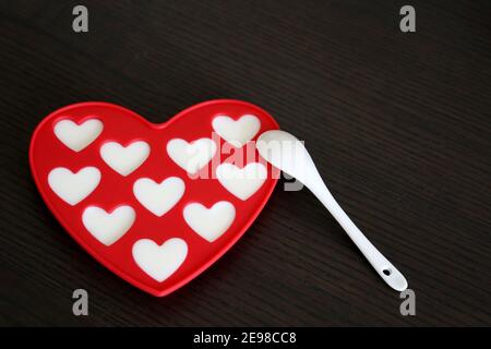 Creamy dessert for Valentine's Day, romantic breakfast. Heart-shaped red silicone mold and white spoon on dark wooden table Stock Photo