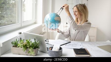 young, beautiful female architect is sitting in her office and is holding a globe and is dreaming of travelling around the world Stock Photo