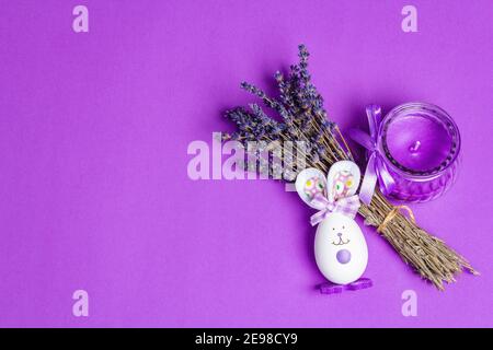 Monochromatic lavender Easter concept. Fragrant flowers, natural purple candle and cute bunny. Matte lilac background, place for text Stock Photo