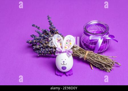 Monochromatic lavender Easter concept. Fragrant flowers, natural purple candle and cute bunny. Matte lilac background, place for text Stock Photo