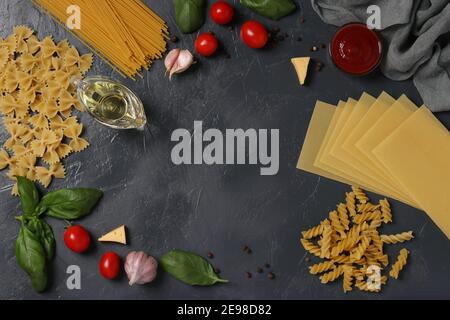 Border of raw pasta durum wheat, tomato sauce, cherry tomatoes, basil and spice on dark gray. View from above. Stock Photo