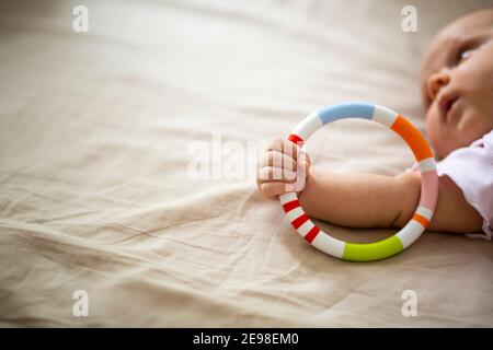 Detail of a newborn's hand holding a colorful toy wheel. Beige background. Face out of focus. Stock Photo