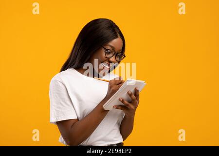 Intelligent black woman in glasses student taking notes on yellow Stock Photo