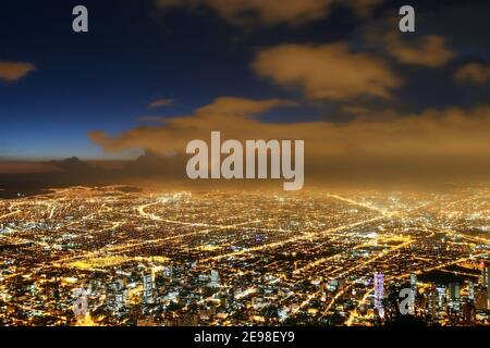 Beautiful aerial view of Bogota city at night with business buildings, street lights, avenues and sky at dusk with clouds in the background. Stock Photo