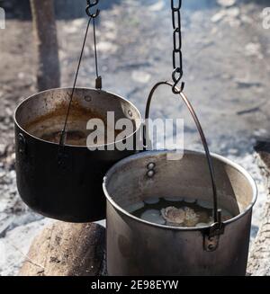 Cooking in two sooty old cauldrons on campfire at forest. Close-up view. Stock Photo