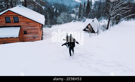 Happy young couple having fun on the mountain in winter. Approaching wooden hut. Stock Photo