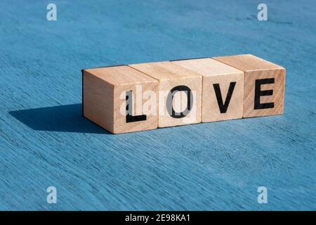 Valentin's day and happy emotion concept: The word LOVE written with single wooden cube letters made for board games on blue textured surface with cop Stock Photo
