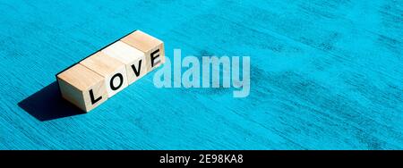Valentin's day and happy emotion concept: On left, the word LOVE written with single wooden cube letters made for board games on blue textured surface Stock Photo