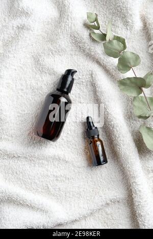 SPA natural organic cosmetics set. Serum and essential oil with eucalyptus leaf on white towel in bathroom. Flat lay, top view. Stock Photo