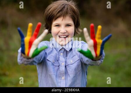 Outdoor portrait of cheerful kid girl show hello gesture with hands painted in Seychelles flag colors Stock Photo