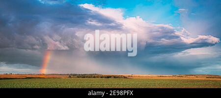 Dramatic Sky During Rain With Rainbow On Horizon Above Rural Landscape Field. Agricultural And Weather Forecast Concept. Countryside Meadow In Rainy Stock Photo