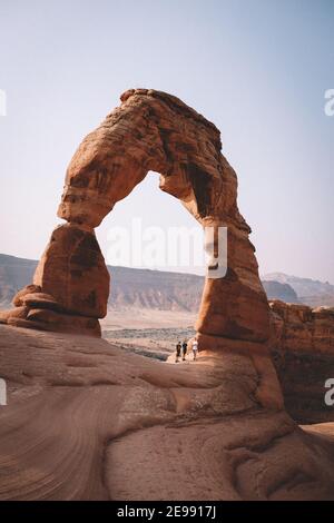 Three Friends on an adventure stand under the Delicate Arch. Stock Photo