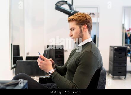 young man using his smartphone at the hairdresser Stock Photo