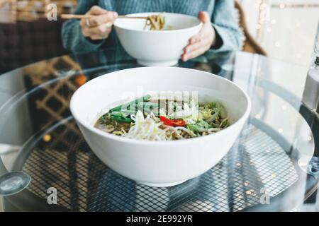 Close-up of a plate with ramen noodle soup. Asian traditional food. The girl is eating in the background. Stock Photo