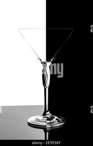 Empty transparent martini glass on mirrored surface over black and white background, studio advertising shot, copy space Stock Photo