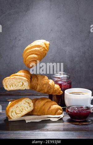 cup of coffee, jam and flying croissants on a dark background. French breakfast. Stock Photo