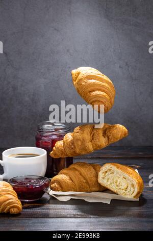 cup of coffee, jam and flying croissants on a dark background. French breakfast. Stock Photo