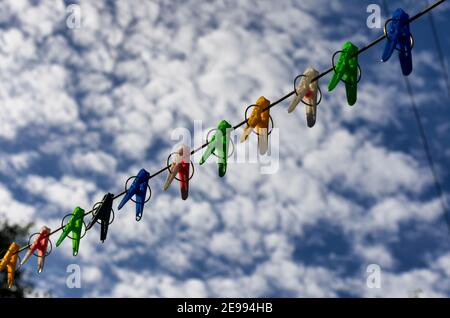 Colorful clothespins on a rope in the background of a blue sky with clouds Stock Photo