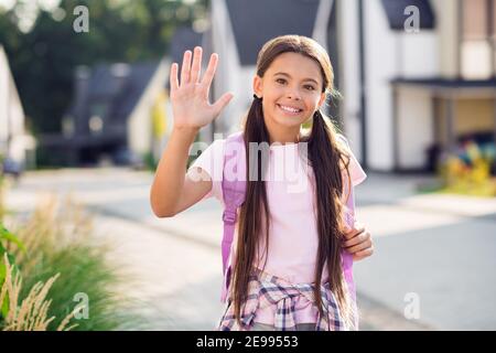 Photo portrait of little girl waving hand saying hello wearing rucksack outdoors Stock Photo