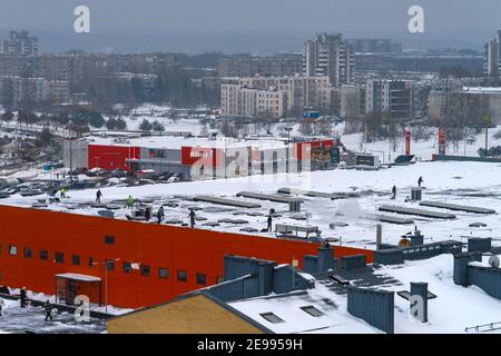 Vilnius, Lithuania- February 03, 2021: Workers cleaning roof of shopping center building from snow with shovels Stock Photo