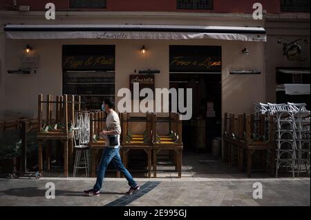 February 3, 2021, Malaga, Spain: A man wearing a face mask as a precaution against the spread of covid-19 walks past tables and chairs stacked at an empty 'Uncibay' square amid the partial lockdown caused by coronavirus pandemic. (Credit Image: © Jesus Merida/SOPA Images via ZUMA Wire) Stock Photo