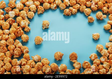 Popcorn is scattered on a blue background, in the form of a frame. Yummy for the filming of movies, TV series, cartoons. Free space, top view Stock Photo