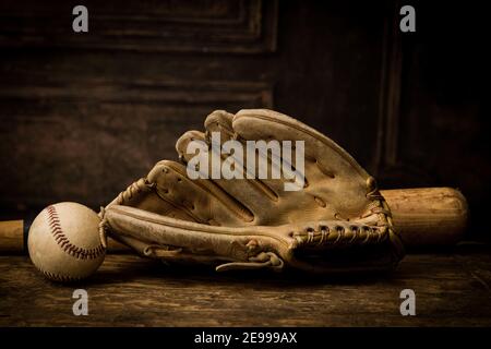 Old leather baseball glove lying on an antique table with ball and bat Stock Photo