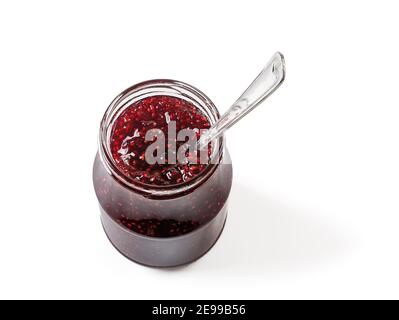 Spoon in open jar full of delicious sweet raspberry jam isolated on white background. Traditional homemade red berry jelly, marmalade or confiture. Stock Photo