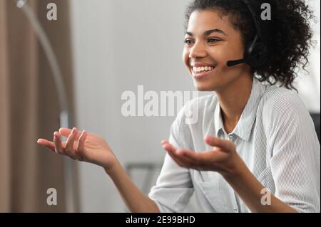 Portrait of excited laughing African American gamer girl or a customer service agent in wireless headphones, headset with a microphone gesturing and Stock Photo