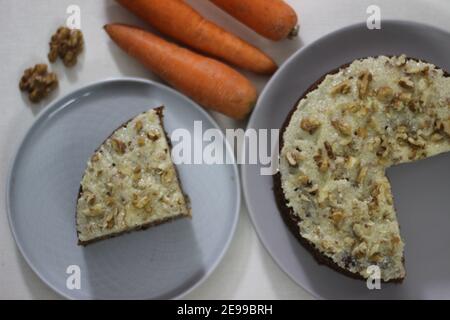 Carrot walnut cake topped with a thin layer of butter, sugar and crushed walnuts. Photographed with carrots on white background Stock Photo