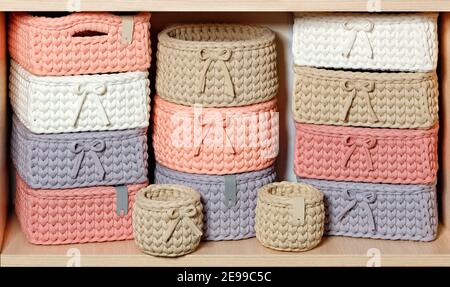 Multi-colored wicker textile baskets for storing women's jewelry on a wooden shelf, close-up. Stock Photo