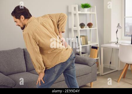 Young man standing at home touching lower back and suffering from pain Stock Photo