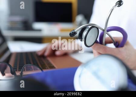 Doctor holding stethoscope and typing on laptop keyboard closeup Stock Photo