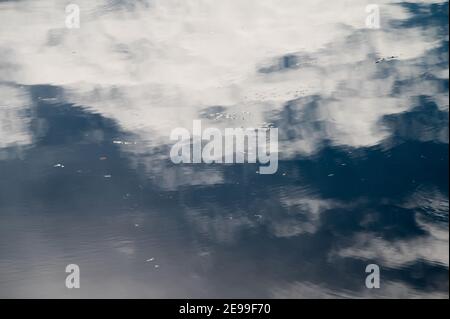 Cloudy sky reflects in lake with small bubbles on water surface Stock Photo
