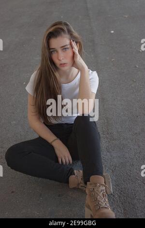 Gorgeous blue eyed brunette young European looking at camera with calm facial expression, posing isolated against street wall background. Stock Photo