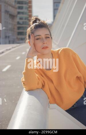 Open picture of a young woman with a yellow sweater posing to the camera on a sunny day in the city center. Spring Photography 2021. Stock Photo