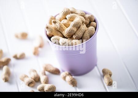 Roasted peanuts. Tasty groundnuts in cup on white table. Stock Photo