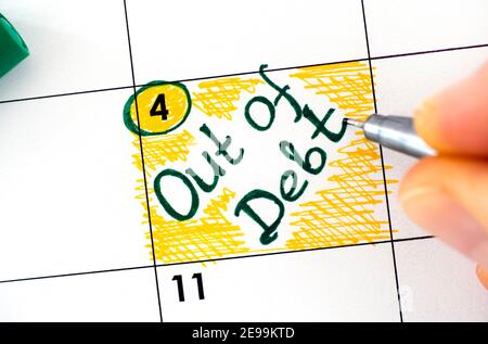 Woman fingers with pen writing reminder Out of Debt in calendar. Close-up Stock Photo