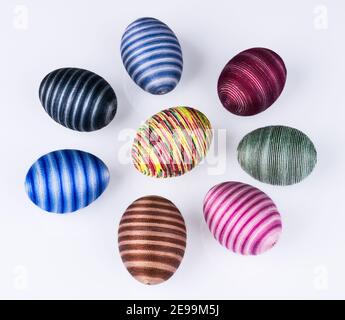 Group of colored Easter eggs with striped pattern on white background. Collection of various hollow shells hand-decorated by pasted sewing cotton yarn. Stock Photo