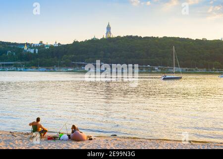 KIEV, UKRAINE - AUGUST 05, 2020: Couple fishing on the beach of Dnipro river. Kiev Pechersk Lavra in the background. Stock Photo