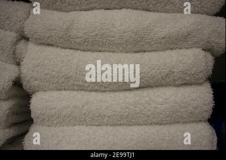 A stack of neatly-folded, clean, white towels sit on a white shelf in a cabinet. Stock Photo