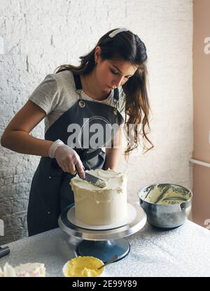 a pastry chef girl in a gray apron makes a cake in the kitchen Stock Photo