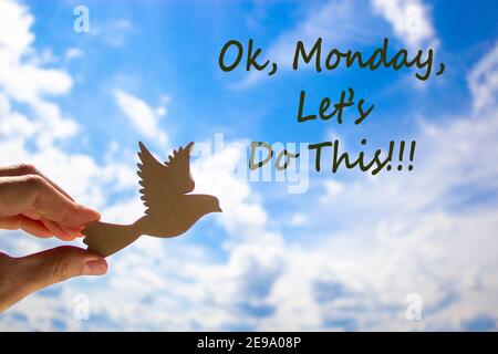 Success start symbol. Man hand holding wooden bird on cloud blue sky background. Words 'ok, monday, let is do this'. Business, support and motivationa Stock Photo