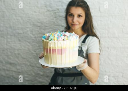 a pastry chef girl holds a prepared cake in her hands. Stock Photo