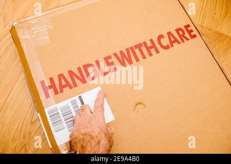 POV male hand pointing with finger at handle with care inscription on the cardboard box of a new parcel delivered by freight transportation service - arranged on the wooden parquet floor in the living room Stock Photo