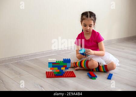 Girl play with multi-colored plastic constructor on floor Stock Photo