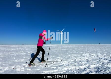 Winter sports, woman cross country skiing, and background man snowkiting under a wind turbine Czech Republic mountains plain Woman skiing Stock Photo