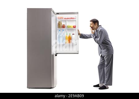 Sleepy man in pajamas yawning and opening a fridge isolated on white background Stock Photo